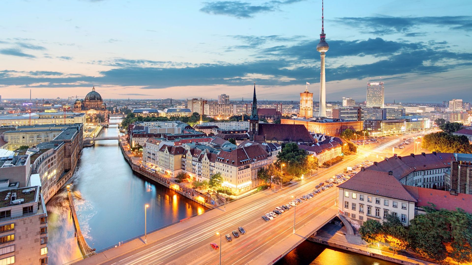 Ein Panoramablick über Berlin in einer warmen Abendstimmung. Unter anderem zu sehen: Reichstaggebäude, die Spree, Alexanderplatz