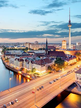 Ein Panoramablick über Berlin in einer warmen Abendstimmung. Unter anderem zu sehen: Reichstaggebäude, die Spree, Alexanderplatz